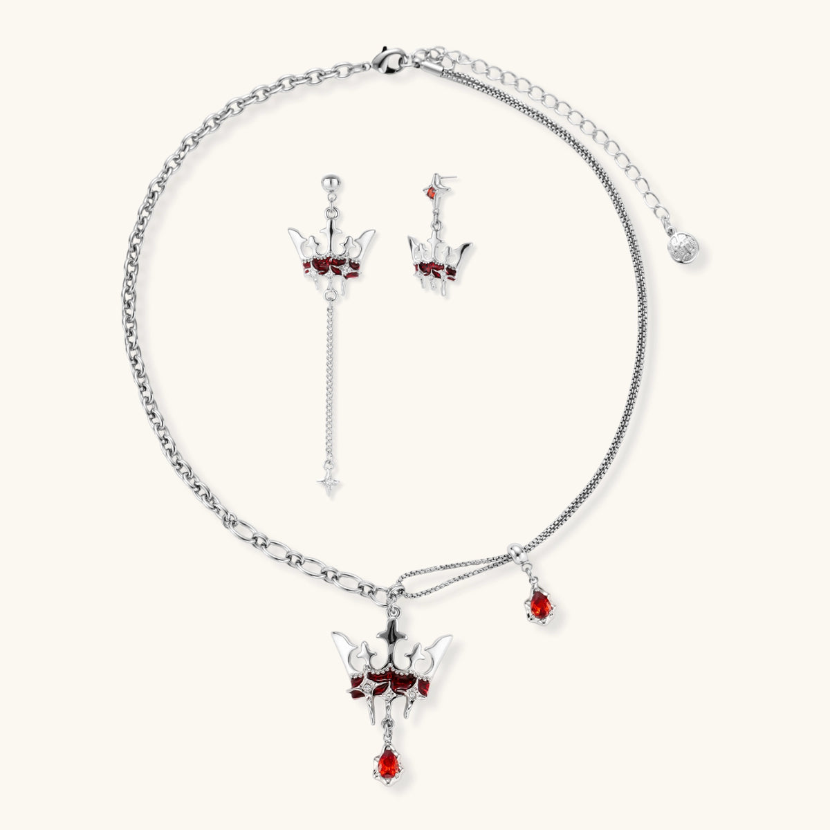 Silver-tone crown pendant with red zirconia stones and matching asymmetrical earrings on cream background