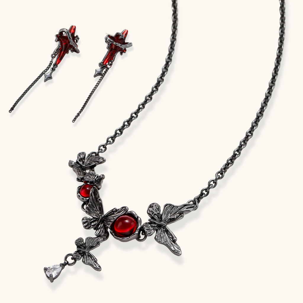Gothic jewelry set with red resin cross pendants wrapped in dark metal chains on cream background.